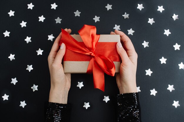 Woman hands holding present box with red bow on black