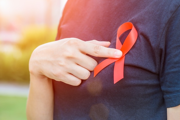 Woman hands holding red AIDS awareness ribbon.