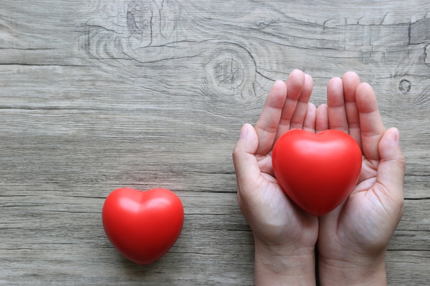 Woman hands holding red heart on wooden table