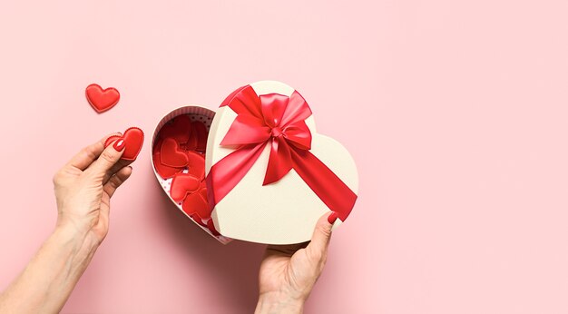 Woman hands holding red hearts from Valentine's Day gift box on pink