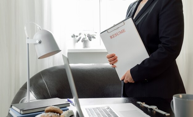 Mani della donna che tengono l'applicazione del curriculum vicino al suo posto di lavoro con il laptop