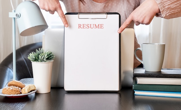 Woman hands holding resume application near her workplace with laptop.