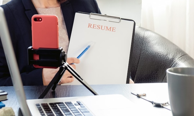 Mani della donna che tengono l'applicazione del curriculum vicino al suo posto di lavoro con il computer portatile.