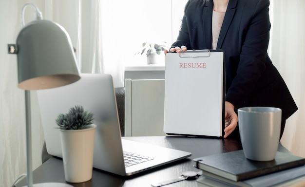 Mani della donna che tengono l'applicazione del curriculum vicino al suo posto di lavoro con il computer portatile.