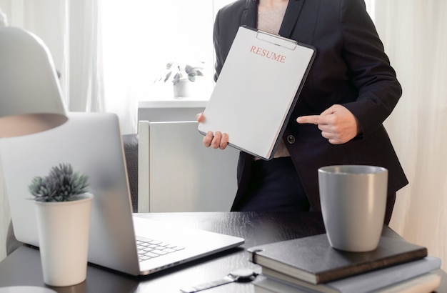 Mani della donna che tengono l'applicazione del curriculum vicino al suo posto di lavoro con il computer portatile.