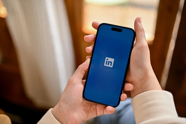 A woman hands holding a smartphone with LinkedIn logo on screen iPhone with LinkedIn logo