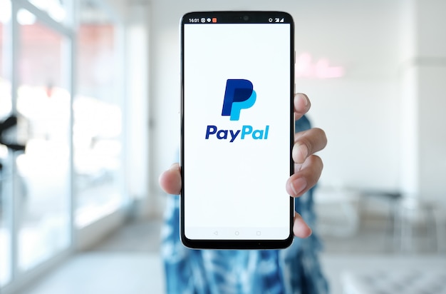 Фото Женщина руки, держа смартфон с paypal приложений на экране. paypal - это онлайн-система электронных платежей.