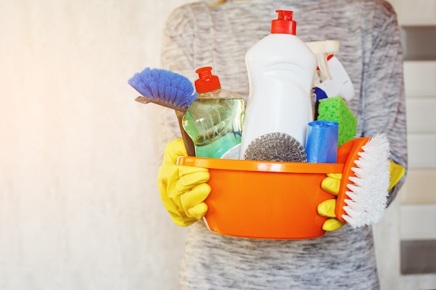 Woman hands holding tub with cleaning supplies.