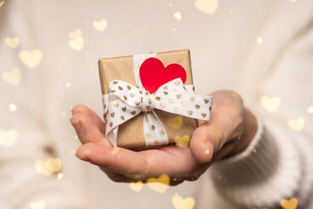 Woman hands holding Valentine Gift with red heart on glow bokeh background