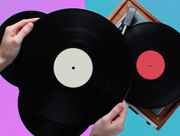 Woman hands holding vinyl record, vinyl player with records on a two-color background. Retro style, 80s, top view