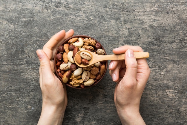 Photo woman hands holding a wooden bowl with mixed nuts walnut pistachios almonds hazelnuts and cashews healthy food and snack vegetarian snacks of different nuts