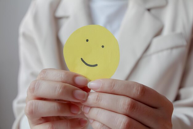 Foto mani di donna che tengono un sorriso giallo viso carta buona valutazione di feedback pensa recensione positiva del cliente