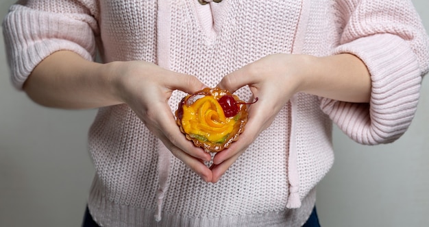 여자는 딸기와 오렌지가 든 맛있는 컵케이크를 들고 심장 모양을 만들고 있습니다. 근접 촬영