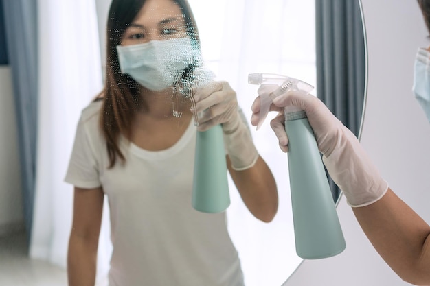 写真 自宅の寝室の鏡面を掃除するために洗剤を噴霧するゴム製の保護手袋をはめた女性の手クローズアップ