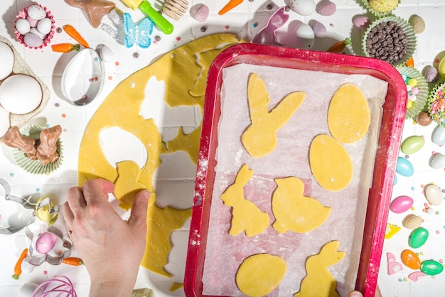 Woman hands kneading dough on table and cooking Easter sugar cookies Easter baking background with colorful chocolates candy eggs baking utencils ingredients Top view