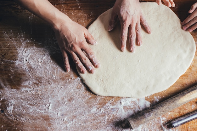 Mani della donna che impastano pasta sul tavolo