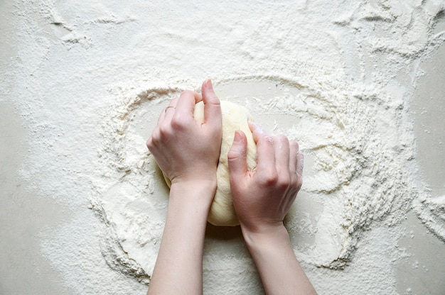 写真 女性の手は白いキッチンテーブルの上に小麦粉で生地をこねます。トップビューフラットレイ。