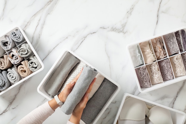 Woman hands neatly folding underwears and sorting in drawer organizers on white marble background