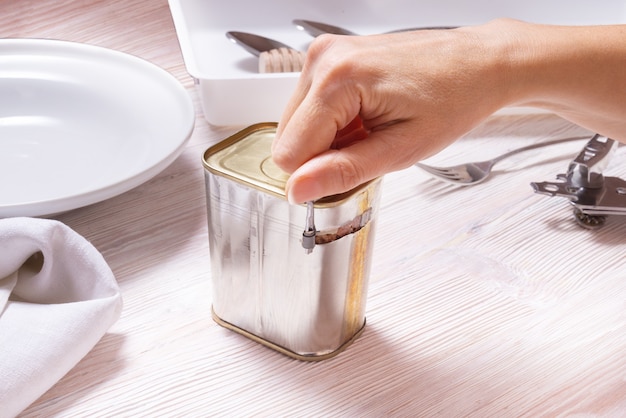 Woman hands opening tin can with corned beef, top view kitchen table