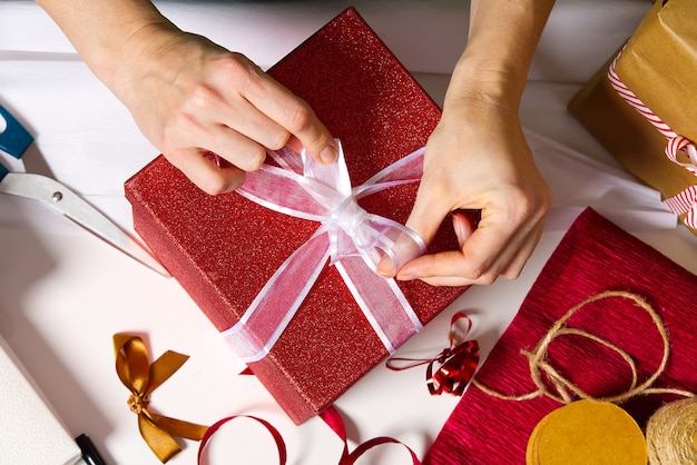 Mani della donna che imballano un regalo di natale in una scatola rossa con un nastro bianco. confezione regalo fai da te