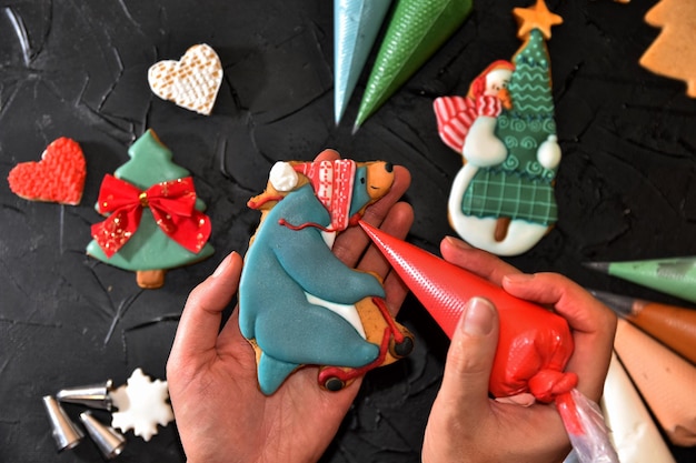 Photo woman hands paint ornaments on xmas treats christmas preparations hands decorate handmade christmas gingerbread with glaze icing sugar female hands paint christmas gingerbread cookies top view