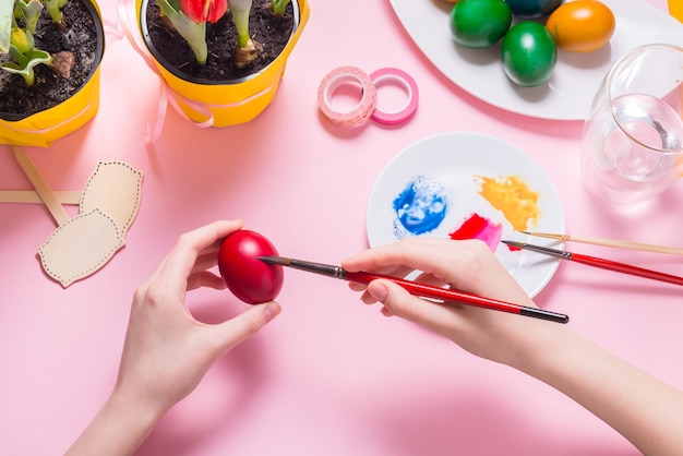 Woman hands painting Ester eggs on pink desk