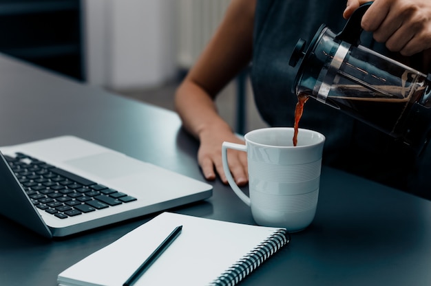 女性の手がオフィスのテーブルの上にカップにコーヒーを注ぐ。