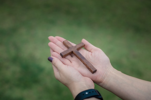 Руки женщины молятся богу с деревянным крестом