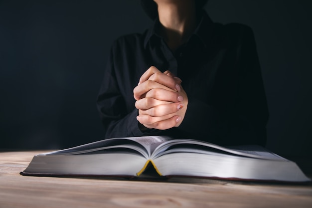 Woman hands praying with a Bible on dark room