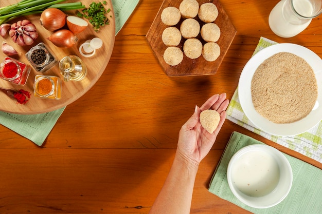 Woman hands preparing brazilian croquette coxinha de frango with bread crumbs on a wooden kitchen table Top view