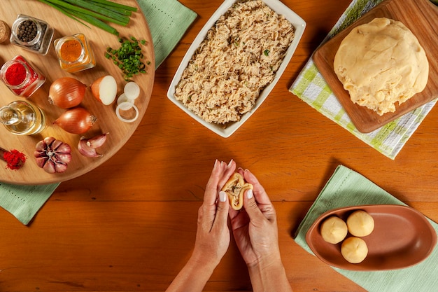 Foto mani di donna che preparano crocchette brasiliane coxinha de frango su un tavolo da cucina in legno vista dall'alto