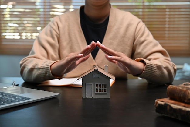 Woman hands protecting small house model. Insurance real estate concept.