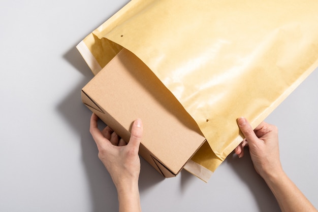 Женщина руки положить картонную коробку внутри большого почтового конверта