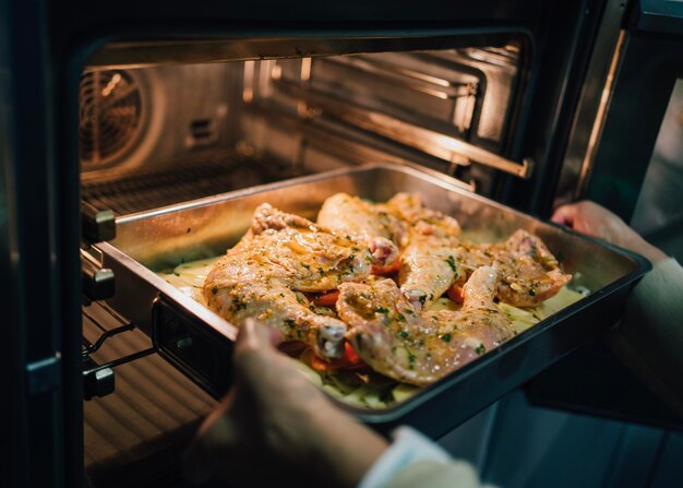 Foto mani di donna che mettono pollo marinato con patate nel forno da vicino