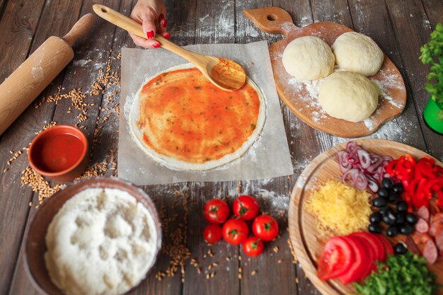 La donna passa mettere la salsa di pomodoro sulla pasta della pizza