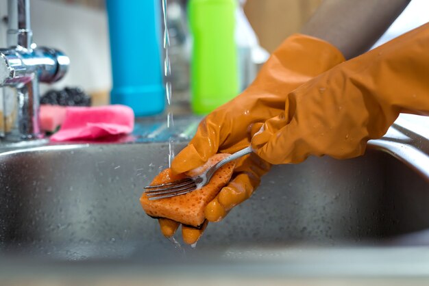 La donna passa la piastra di risciacquo sotto l'acqua corrente nel lavandino. lavori di casa