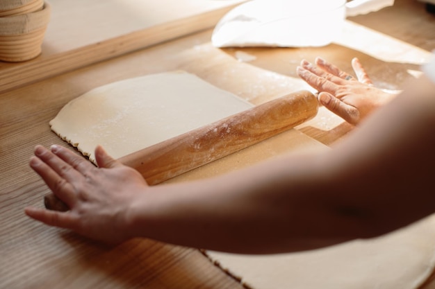 Woman hands rolling out dough in flour with rolling pin in bakery