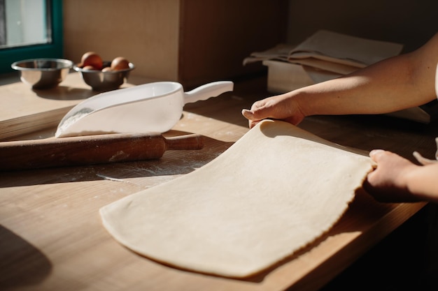 Женщина руками раскатывает тесто в муке скалкой в пекарне