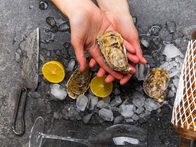 Woman hands take oyster in marble table lemon slices ice wine bottle knife