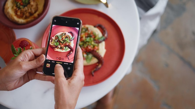 レストランのテーブルで携帯電話を使って美味しい夕食の写真を撮る女性の手