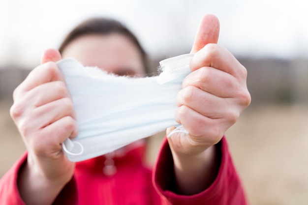 Woman hands tearing apart protective disposable medical face mask End of quarantine and selfisolation due to covid19coronovirus pandemic Exit from home to street Walk in the fresh air in nature