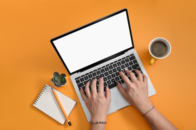 Woman hands typing on laptop computer on yellow background Top view