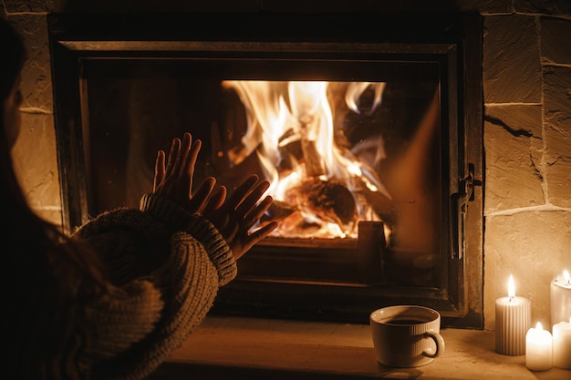 사진 어두운 저녁 방에 있는 아늑한 벽난로에서 여자 손이 따뜻해집니다. 집안의 전기 정전 시 벽난로 난방을 닫습니다. 가정의 노변에서 대기 시간