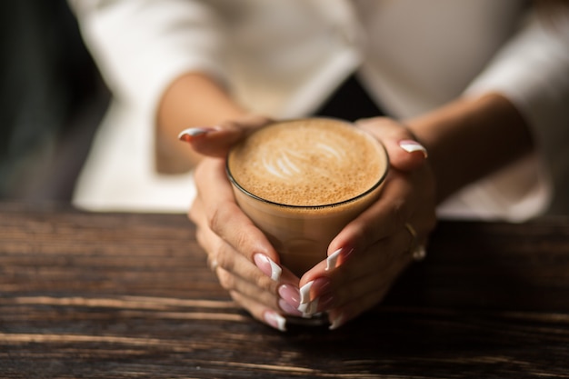 woman hands with beautiful manicure close-up hold a cup with hot coffee on a wooden table