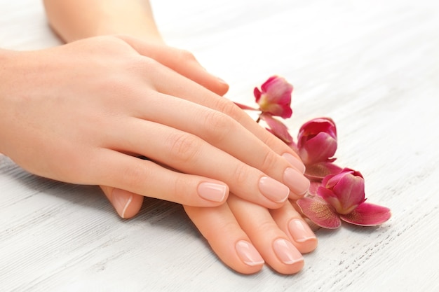 Woman hands with beautiful manicure and purple orchid on wooden background, close up