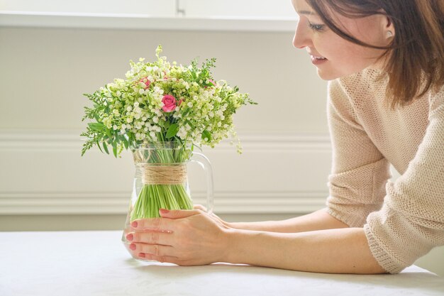 テーブルの上の花瓶に花束と女性の手。スズランとバラの花束、春休み、イースター、母の日を保持している女性