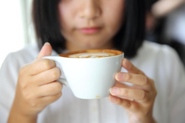 木のテーブルの上のカプチーノコーヒーと女性の手