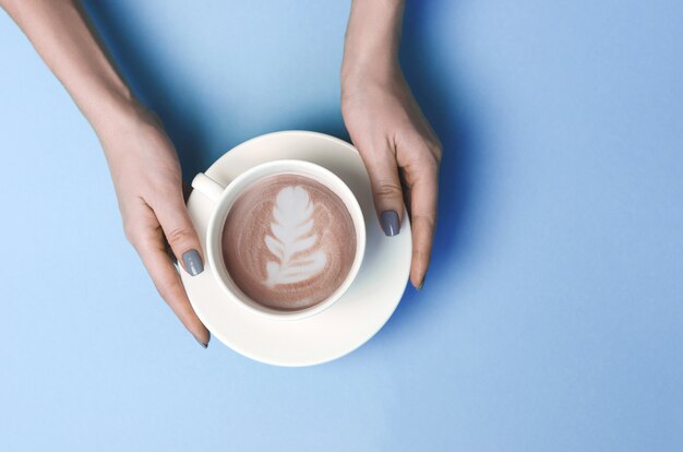 カフェラテアートとコーヒーのカップを持つ女性の手