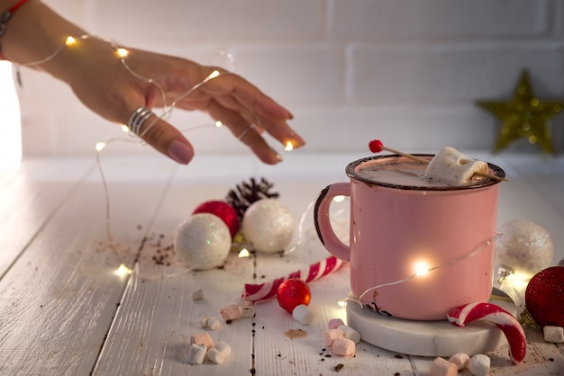 Woman hands with Enamel cup of hot cocoa with mini marshmallows and candy canes 