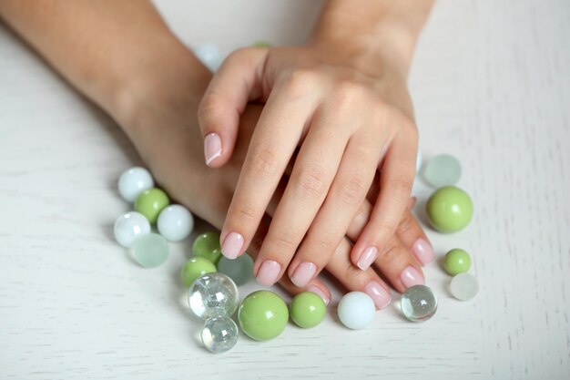 Woman hands with french manicure and glass beads on table closeup